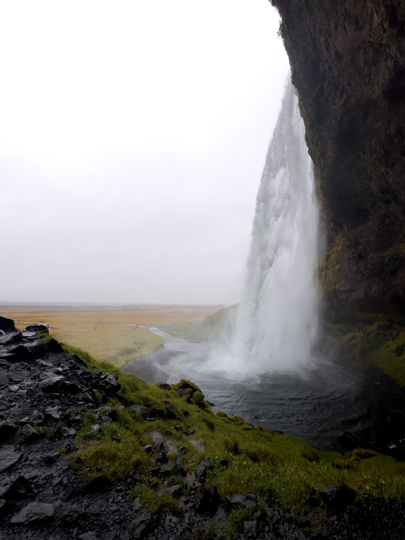 Seljalandsfoss (waterfall) showers down from slightly behind the water in a cave like clearing where you can walk behind the waterfall
