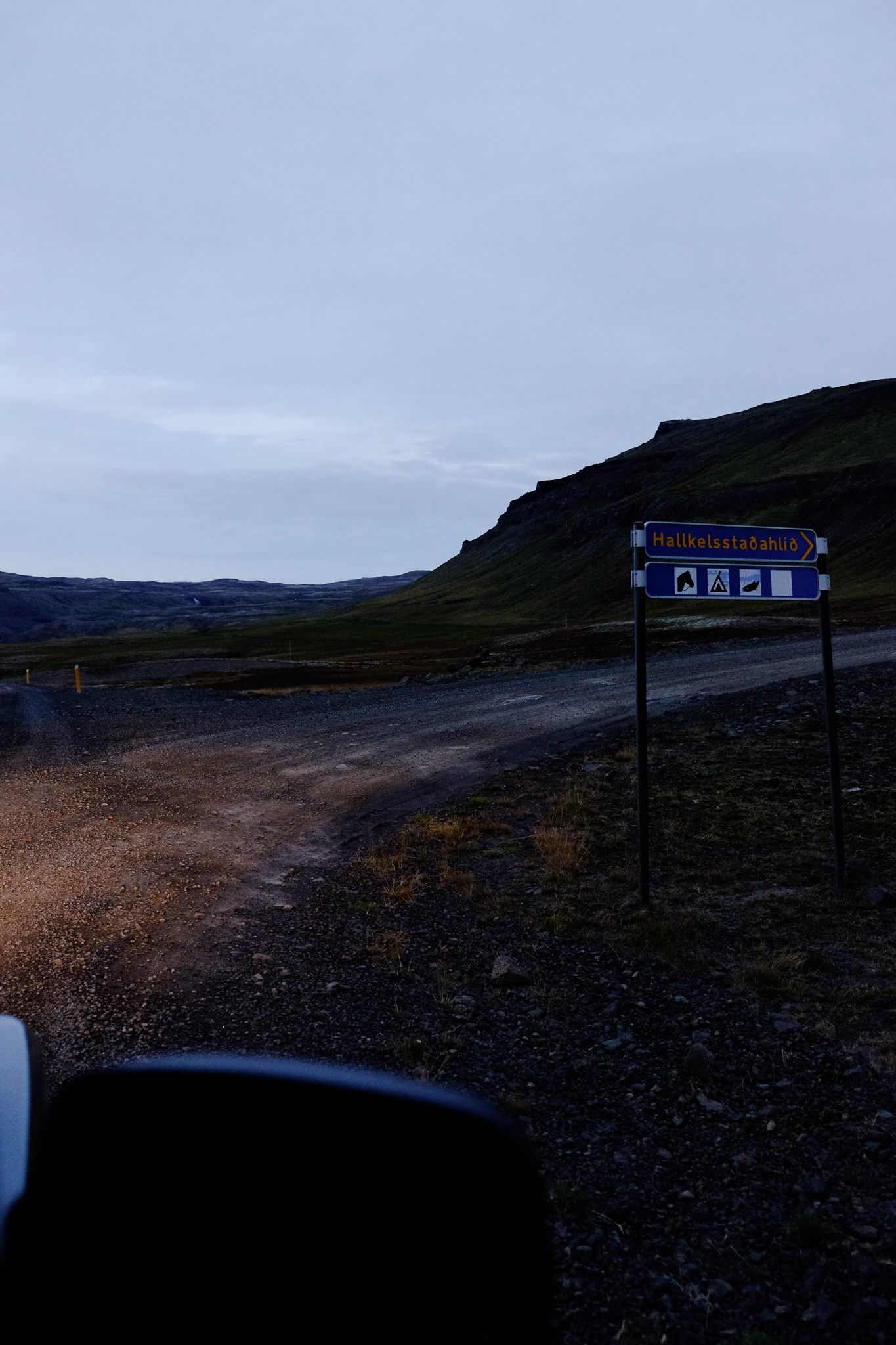 At dusk, a blue sign with yellow writing indicates to turn right towards the farm
