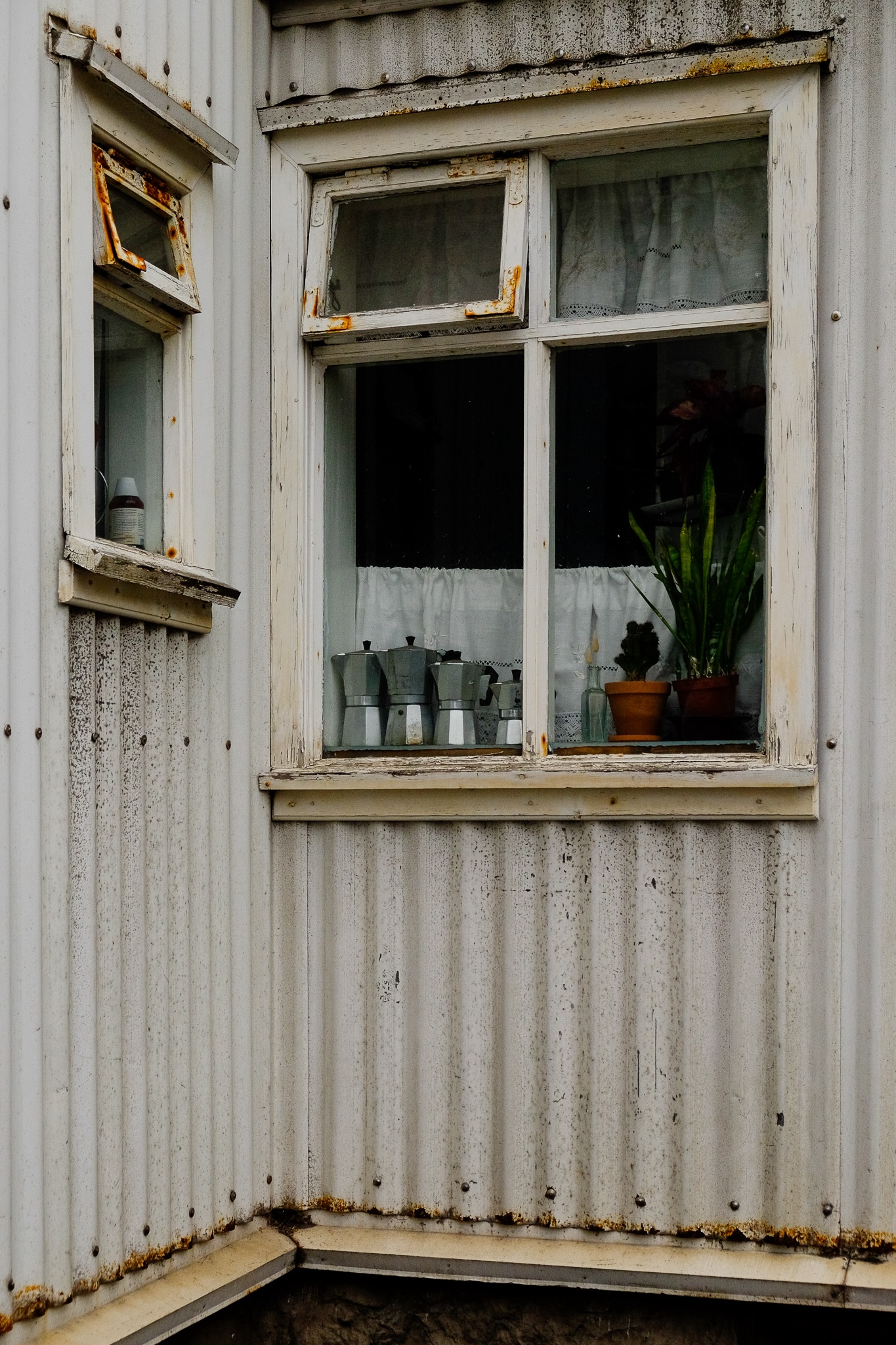 A rusted white corrugated house windowsill has four mochapots of various sizes and two pot plants