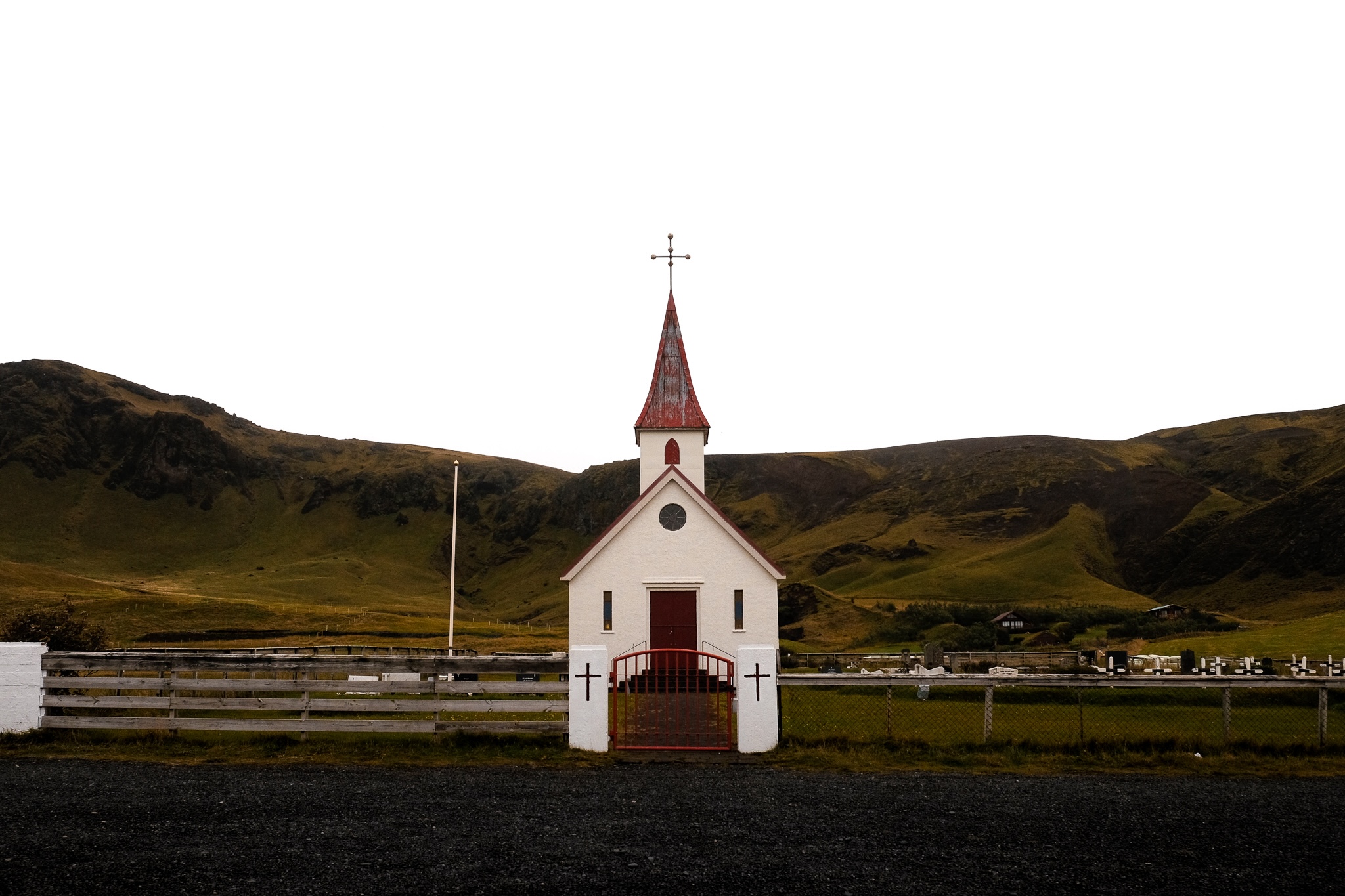 A white church with red trim and a graveyard, against a grassy mountain side