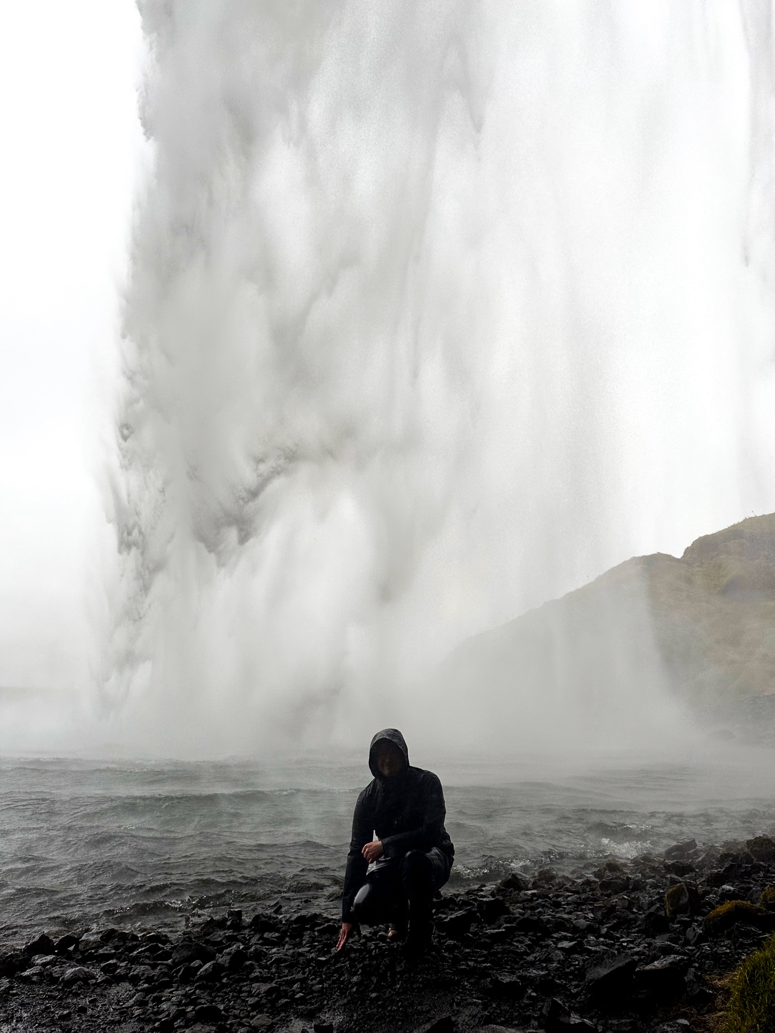 Simon kneels looking towards the camera, completely soaked with a wall of water from Seljalandsfoss pouring behind him
