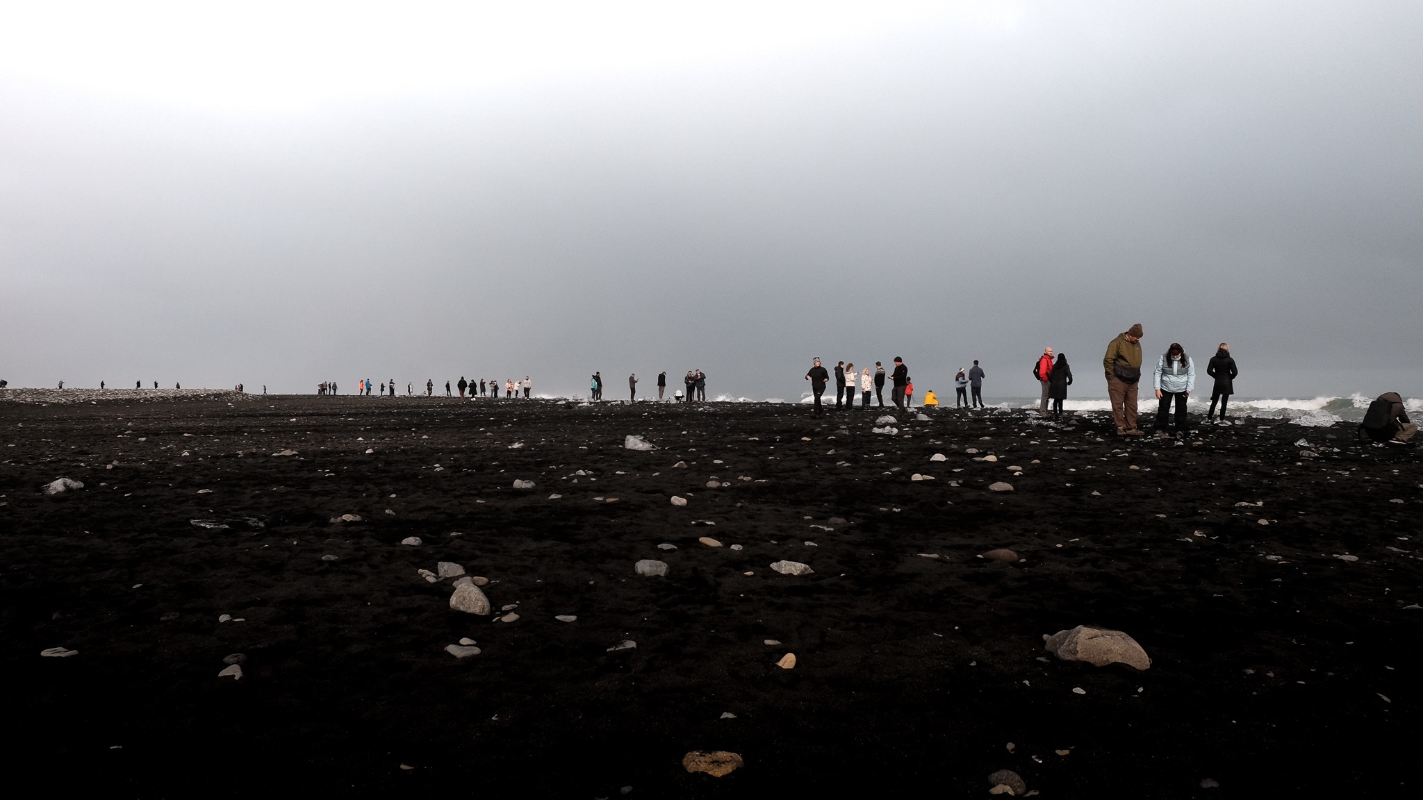 Black beach with tourists inspecting the ice chunks from the glaciel lake that have been pulled out the sea and washed up on the beach, as they melt they reflect the sun and look like diamonds on the black sand