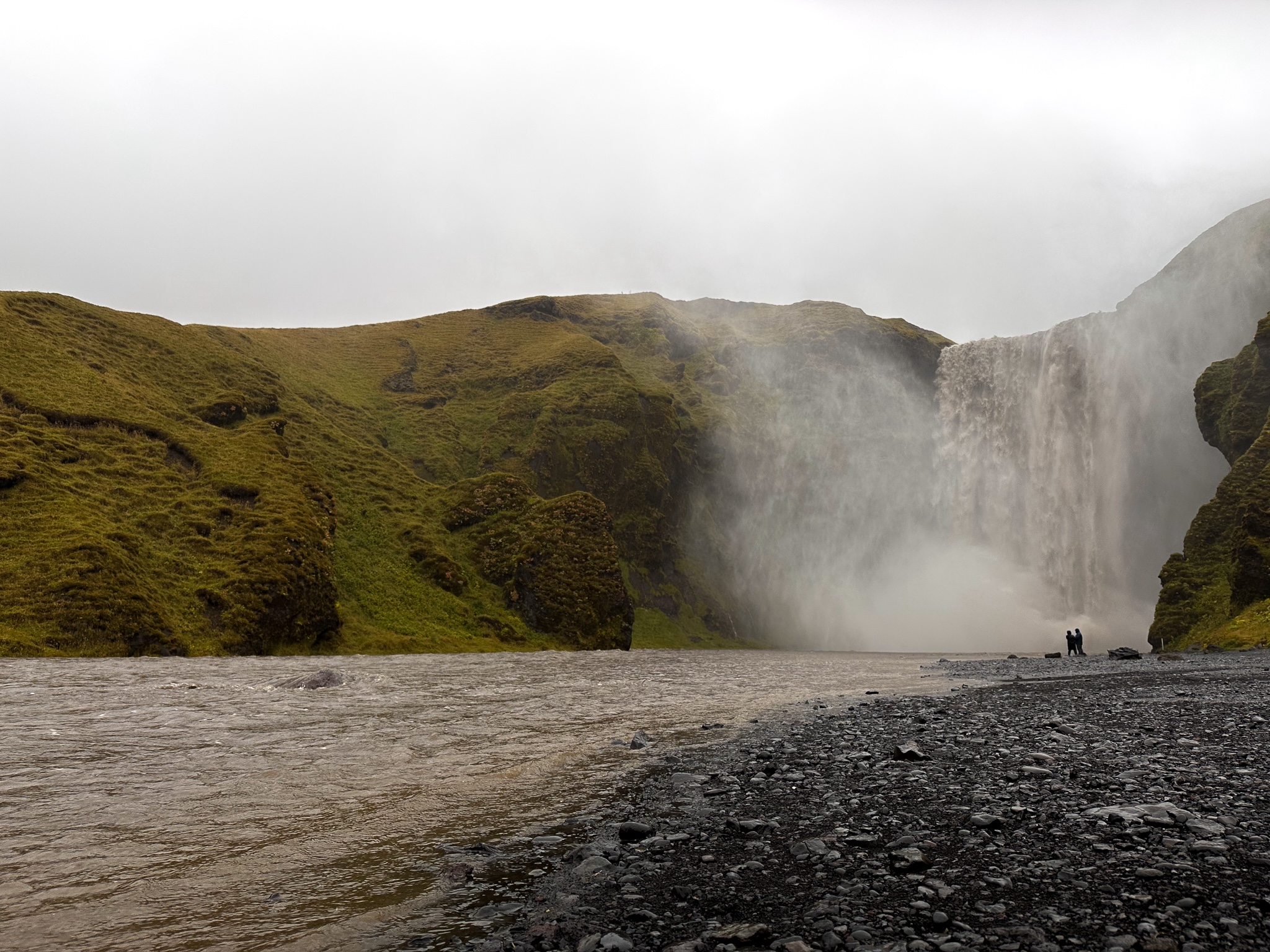 Skogafoss (waterfall) in the rain is brown with a white overcast sky
