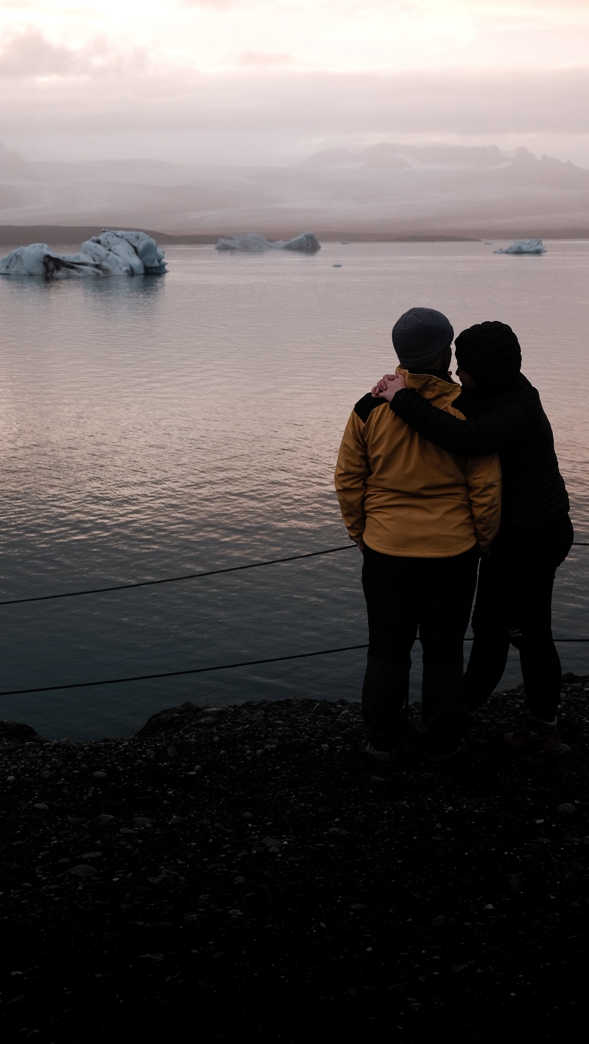 A women leans endearingly against her partner as they look out over the glaciel lake after sunset