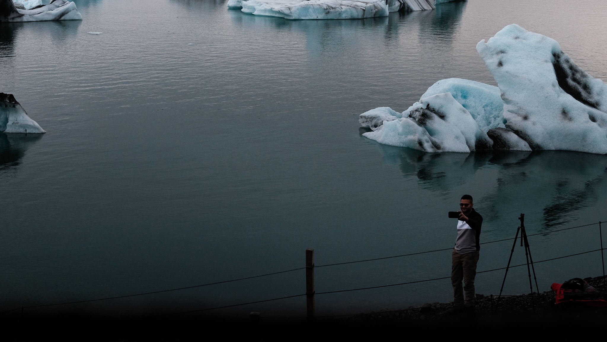 A man standing alone, takes a selfie against the glaciel lake, smiling and capturing the moment for later