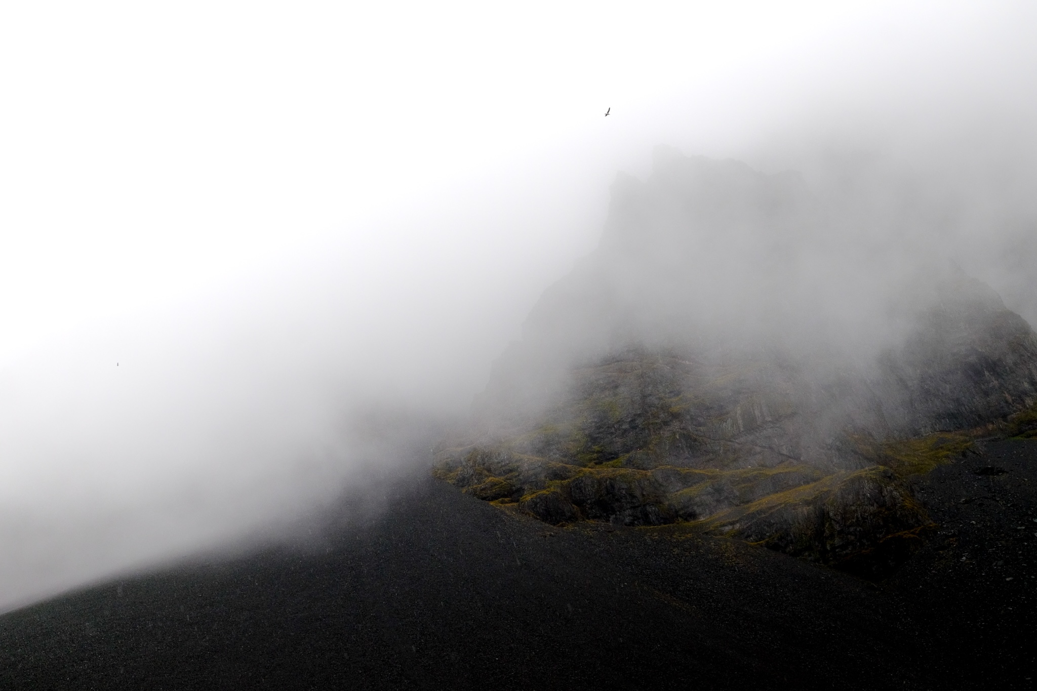 Dark mountain covered in black stones and yellowy-green grass, half covered by thick mist