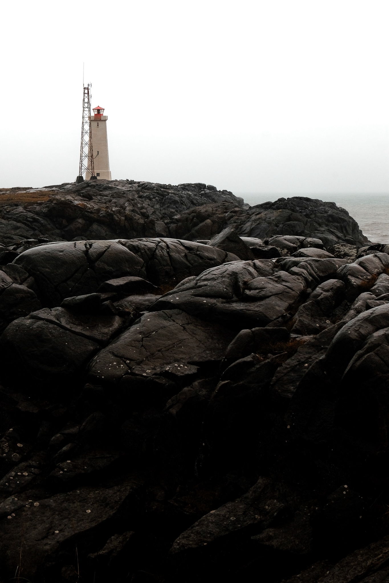 Black rocks with a white lighthouse in the distance against the sea
