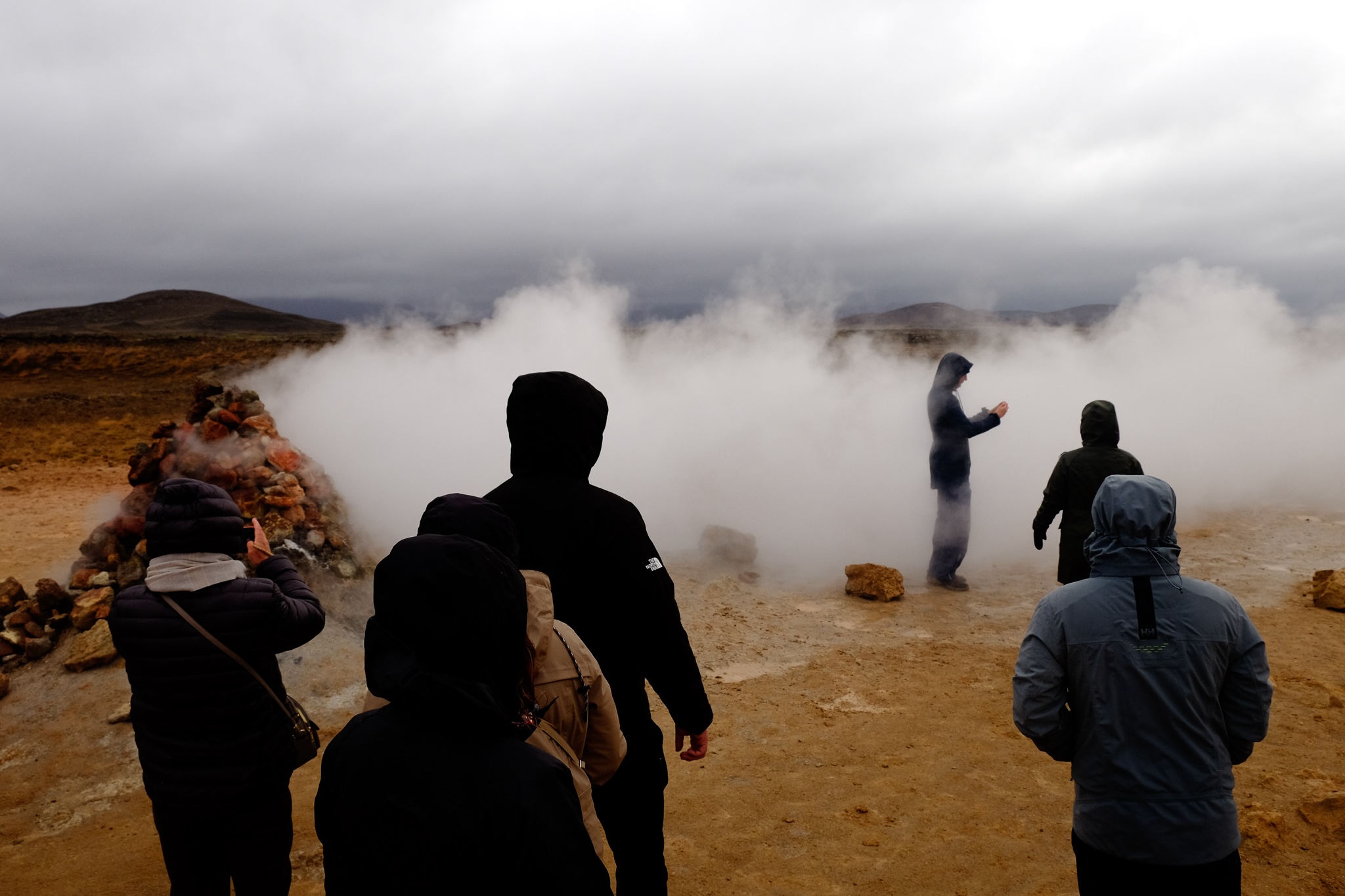 People standing in the steam of a geothermal steam geiser taking photos