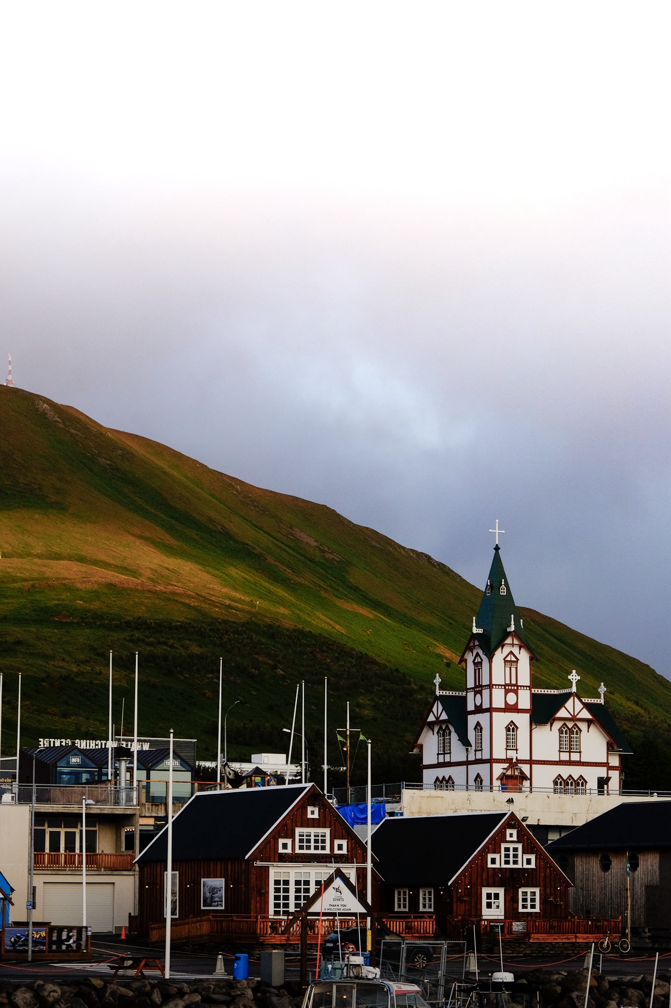White and green church in Husavik taken from the harbour with green mountain side and moody sky in the background