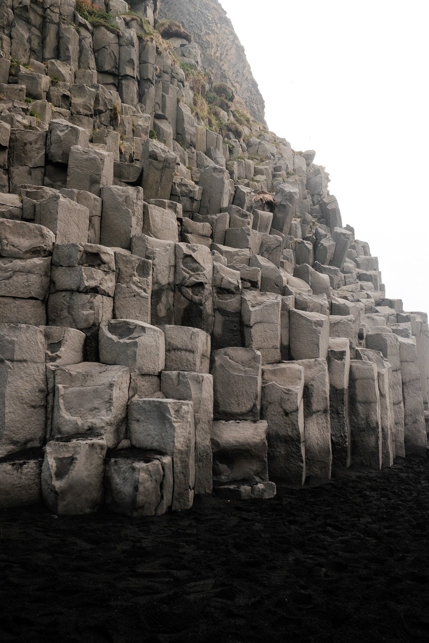 A dirty white basalt rock column formation is the start of the rocky mountain contrasting the black sand of the beach