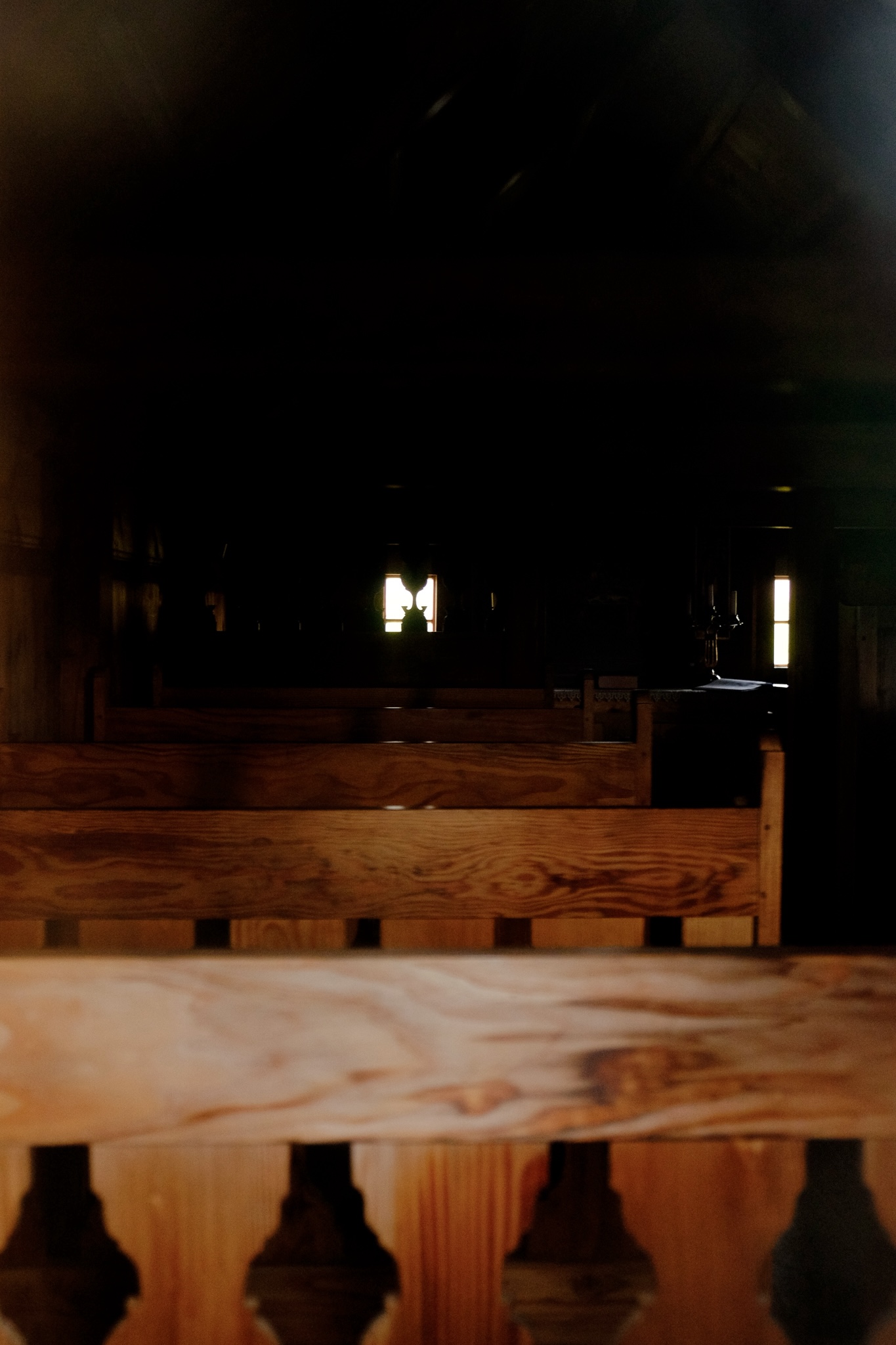 In the window of a church there are wooden pews, the background is dark as the light barely penetrates the interior from the few windows in the church