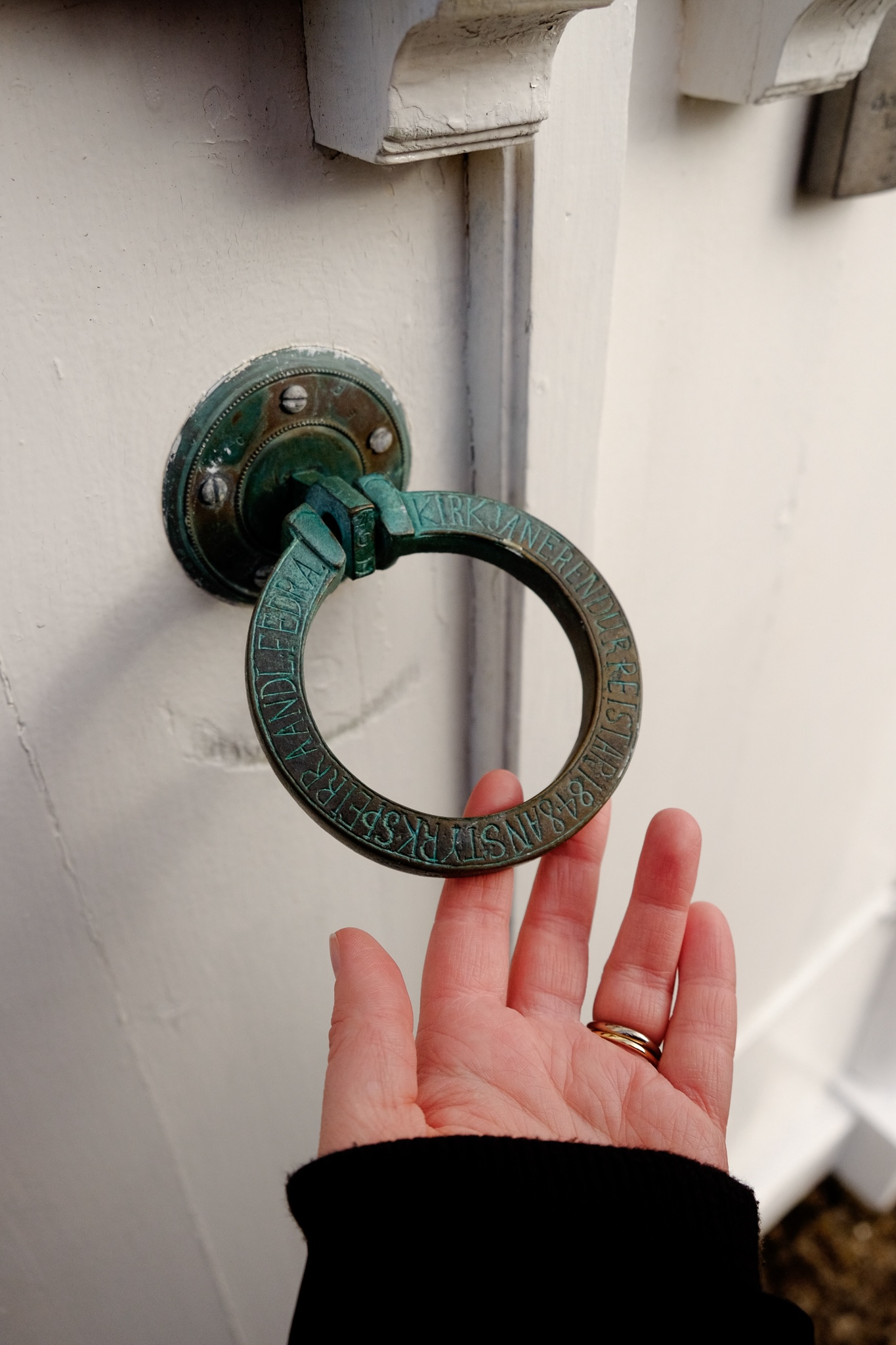 A copper door handle in the shape of a ring turning turquoise through oxidation with an Icelandic inscription etched into it