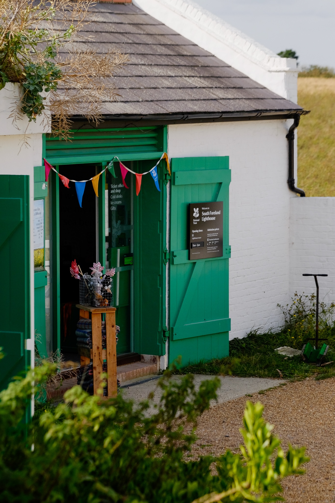 South Foreland Lighthouse ticket office and shop in a white building with bright green wooden doors and multi-coloured flags hanging.