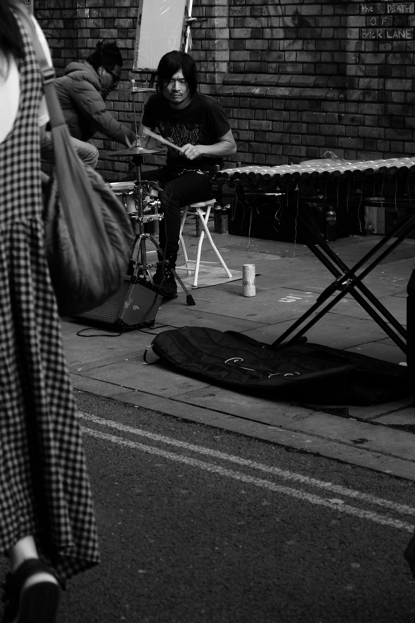 Black and white image of an asian man playing drums on the sidewalk. He rocked a very up-tempo drum and bass rhythm.