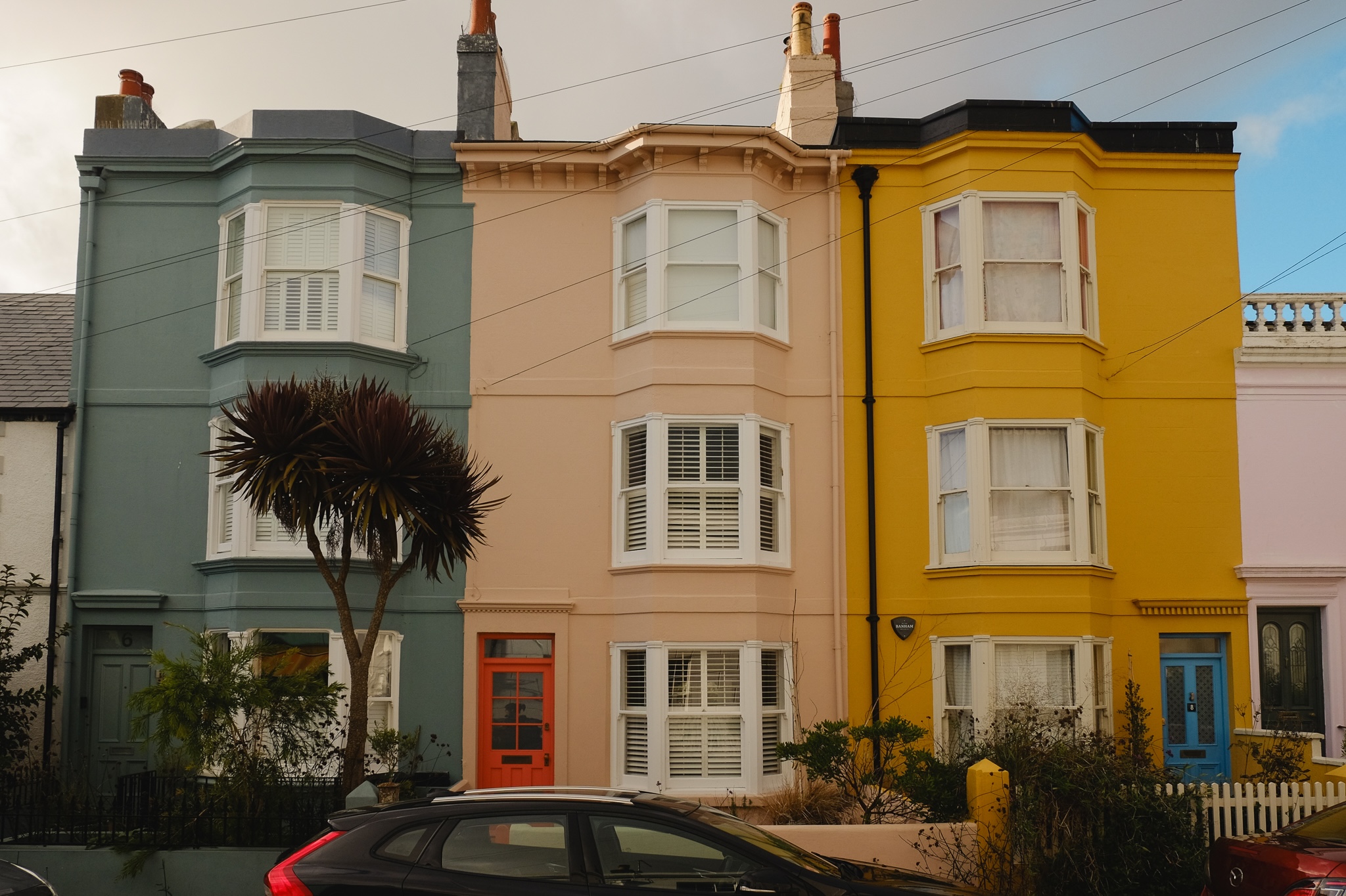 Three houses of the same architecture painted bright colours stand next to each other. Each of them with a different colour door.