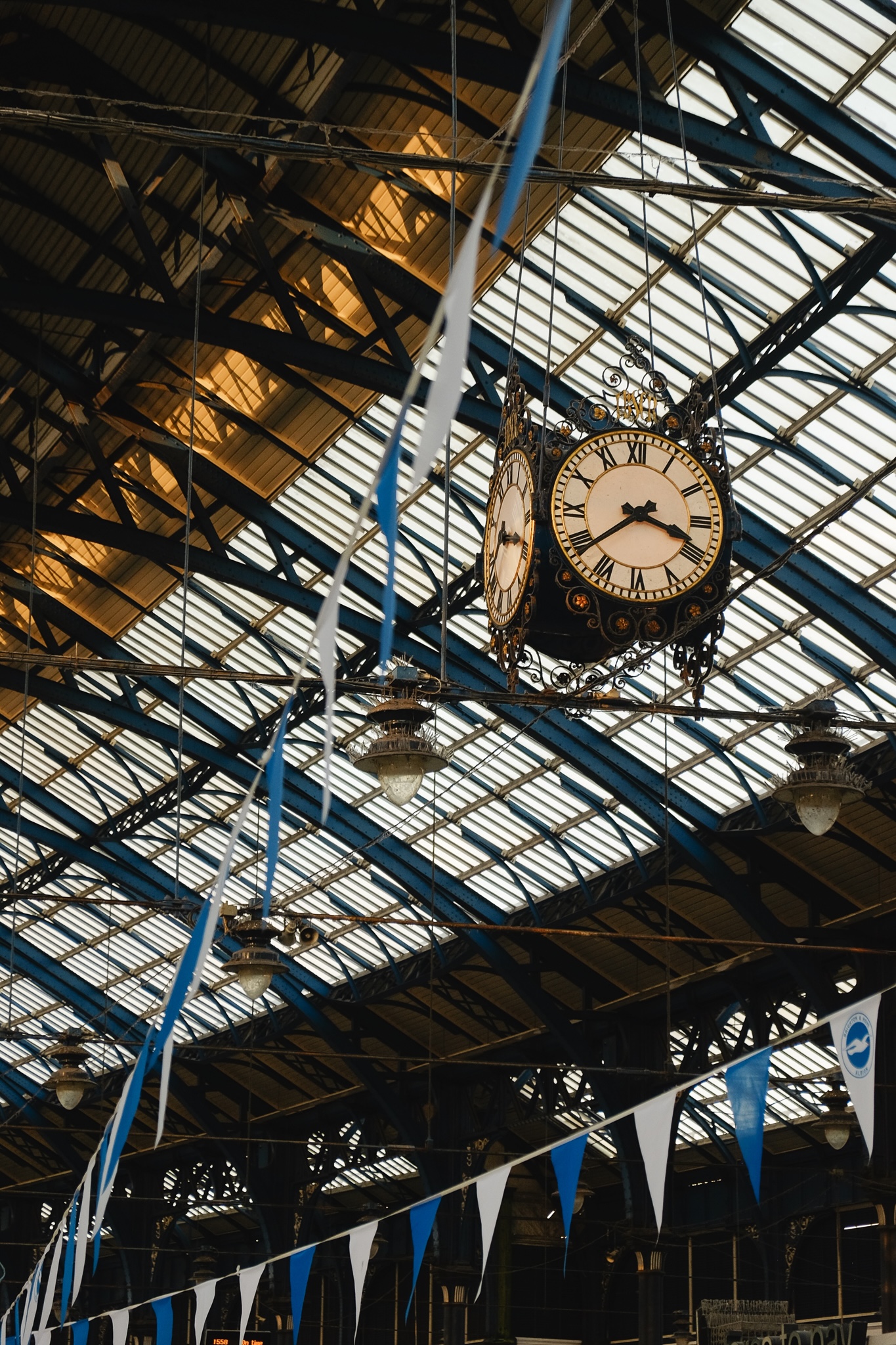 The Brighton train station ornate clock against the steel beams of the enclosing structure with blue and white bunting flags strung across the frame