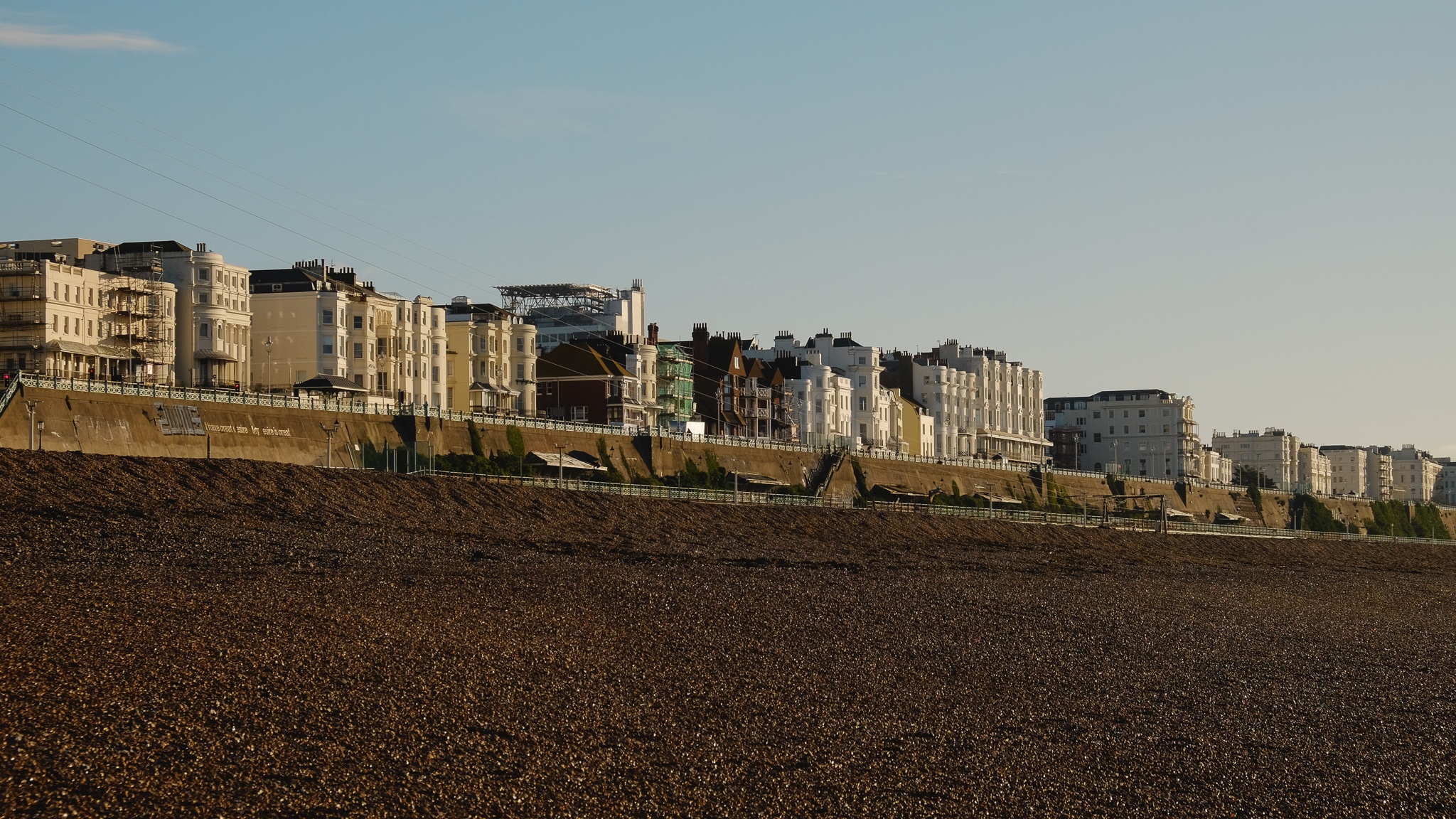 Houses and hotels along the beach being struck by a warm morning light, the pebbled beach in the foreground