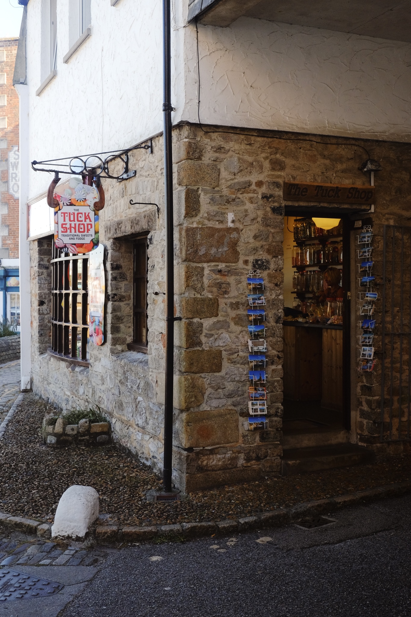 Colourful Tuck Shop sign on a stone building with warm light shining through the door