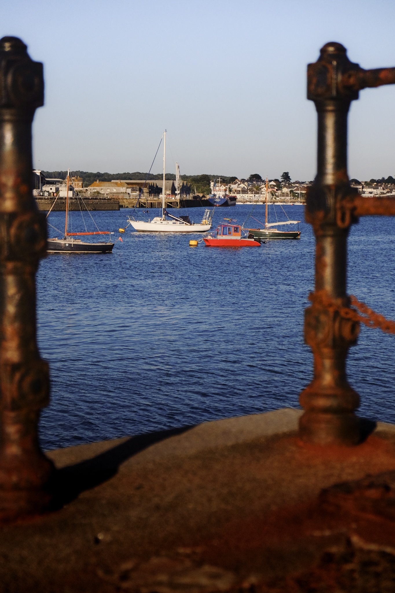 Colourful sailing boats moored in the middle of the harbour with rusted black gate in the foreground