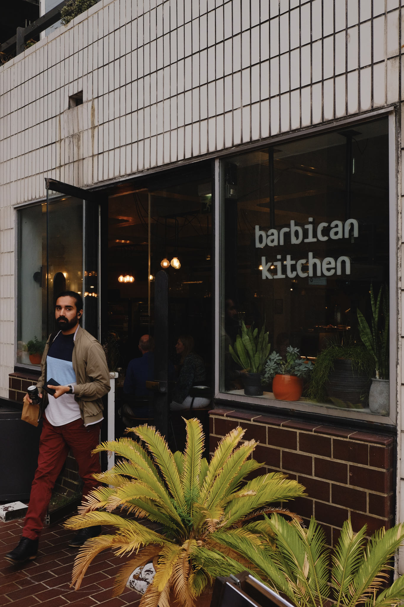 The Barbican Kitchen in white text on the glass of a mid-centry style tiled and brick building